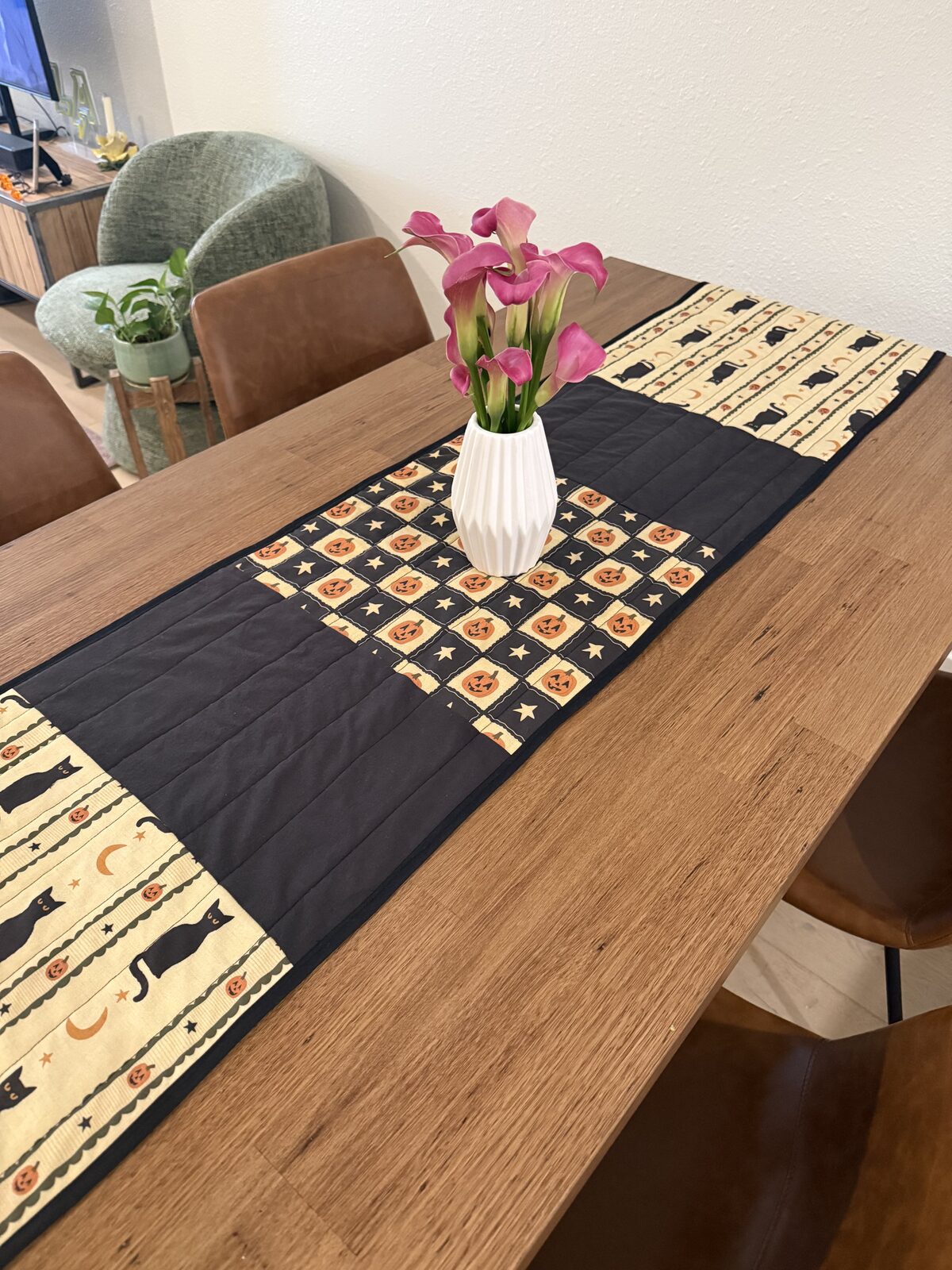 Close up of the runner on the table, showing the quilting lines in the black blocks and the jack o'lantern block under a vase of pink calla lilies